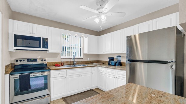 A kitchen with white cabinets, a stainless steel refrigerator, a microwave, an oven, and a ceiling fan. - Spacious 5BR Getaway-Great for Families & Groups (Lauderdale Lakes)