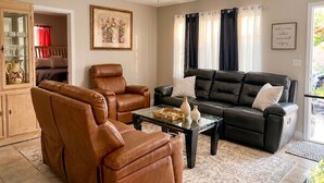 A living room with a sofa, two armchairs, a coffee table, a ceiling fan, a cabinet with glass doors, and a framed picture on the wall. - Spacious 5BR Getaway-Great for Families & Groups (Lauderdale Lakes)
