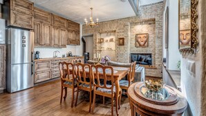 A spacious kitchen with wooden cabinets, a dining area with a wooden table and chairs, and a stone wall with artwork. - House of Nobles with personal terrace in Užupis (Vilnius)