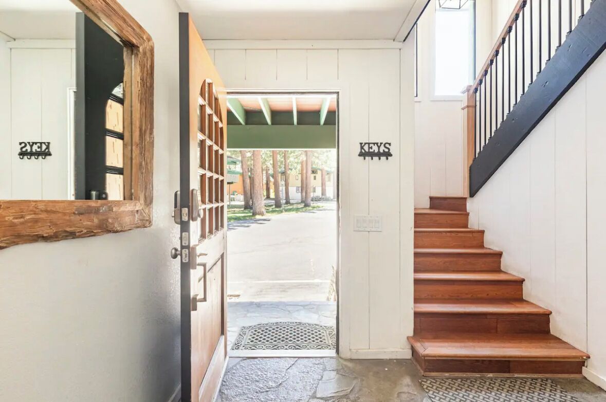 A wooden staircase leading to a door with a metal gate, a sign reading "KEYS" above it, and a view of a covered outdoor area with trees.