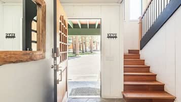 A wooden staircase leading to a door with a metal gate, a sign reading "KEYS" above it, and a view of a covered outdoor area with trees.