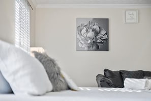 Een slaapkamer met een bed, kussens, een kunstwerk aan de muur en een ingelijste quote.