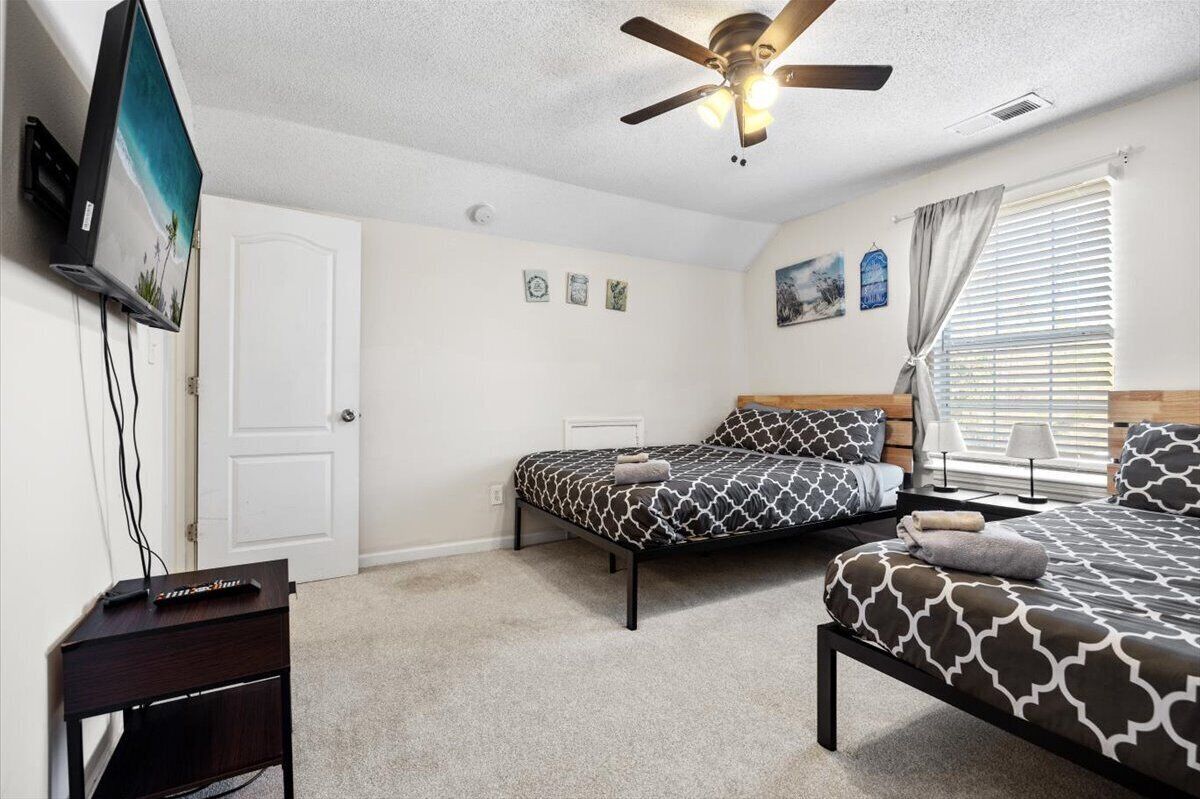 A bedroom with two beds, a ceiling fan, a TV, and a desk.