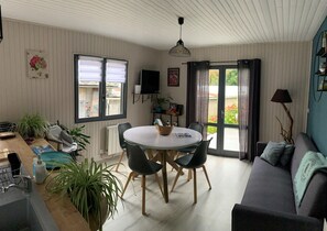 Ein gemütliches Wohnzimmer mit einem runden Esstisch, bequemen Sitzgelegenheiten, einer Couch und Blick durch eine Glastür ins Freie.