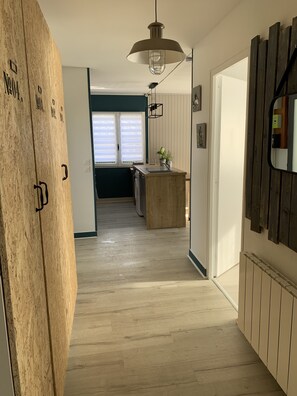 Ein Flur, der zu einer Küche mit einem Holzkasten, einer Pendelleuchte und Blick in den angrenzenden Raum führt.