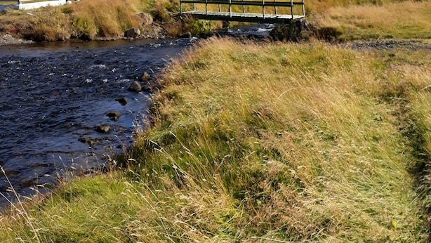 A church with a tall steeple and a small bridge over a stream in a hilly landscape. - Charming 2-bed Cottage Near Seljalandsfoss (Rangárþing eystra)