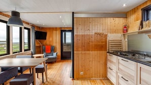 A modern kitchen with wooden walls, a dining area with a table and chairs, and a view through large windows. - Charming 2-bed Cottage Near Seljalandsfoss (Rangárþing eystra)