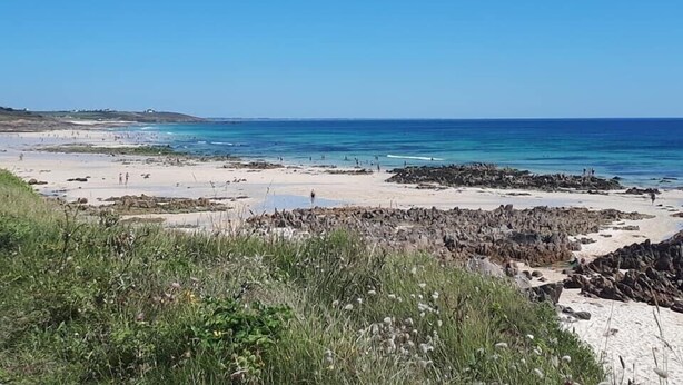 A coastal beach with rocky outcrops and clear blue waters.