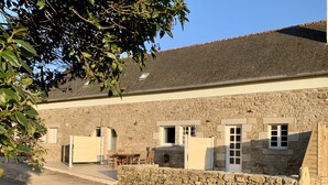 A stone building with a dirt path leading to a wooden table and chairs.