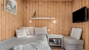 Ett mysigt sovrum med en säng, ett nattduksbord med böcker, en tv och en liten hylla med dekorativa föremål.