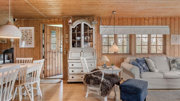 En mysig stuga med en matplats, ett vitt skåp, en soffa och en lampa.