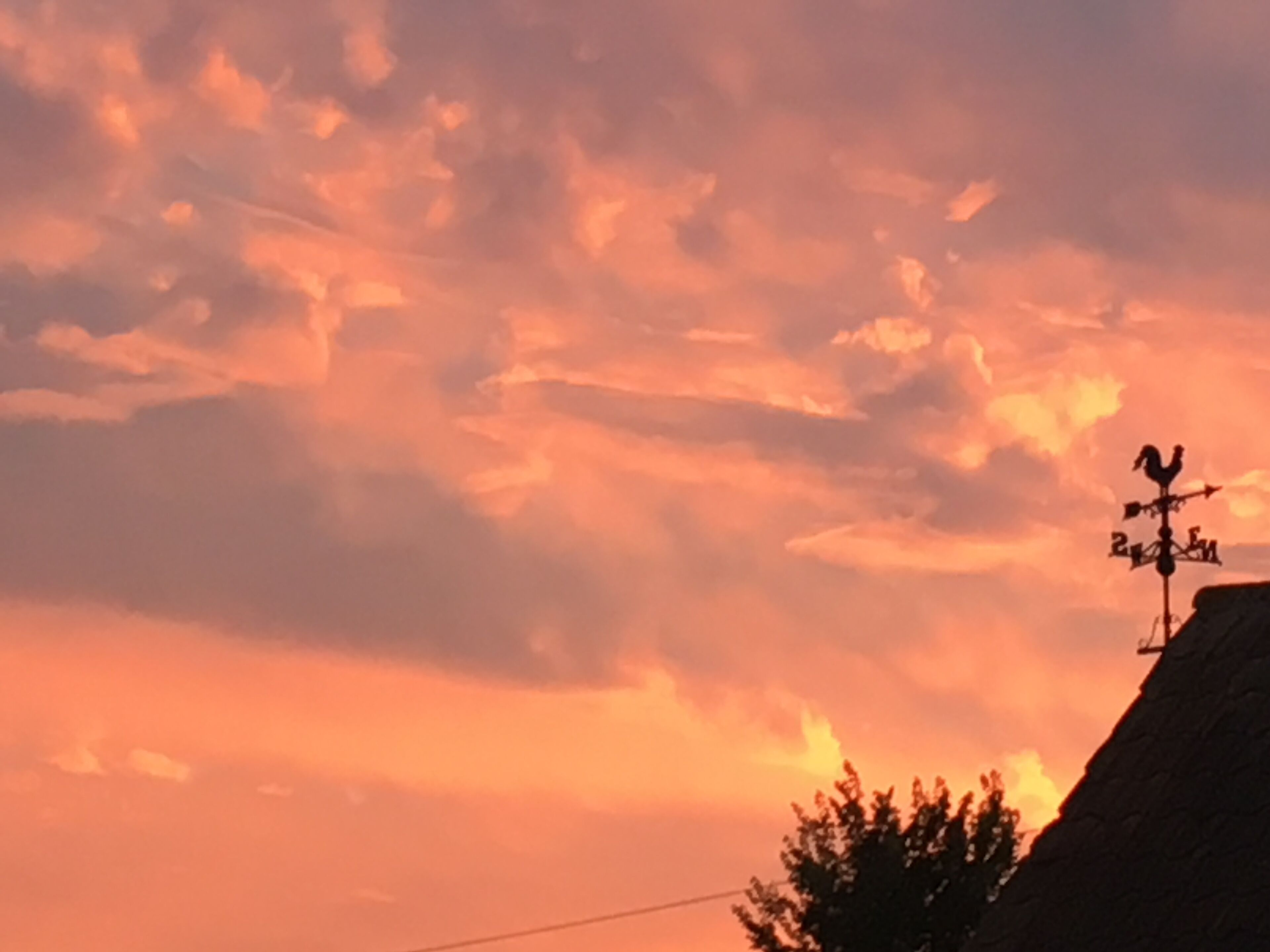 A sunset with clouds and a weather vane on a building.