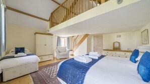 A bedroom with a large bed, a smaller bed, a chair, a dresser, a mirror, and a staircase.