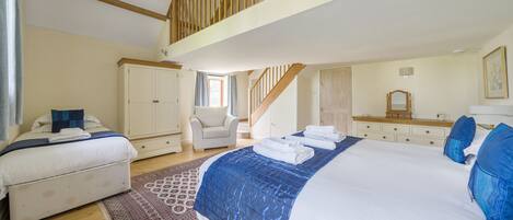 A bedroom with a large bed, a smaller bed, a chair, a dresser, a mirror, and a staircase.