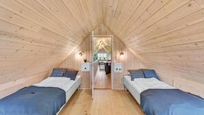 Acogedor dormitorio en el ático con dos camas, paredes de madera y techo inclinado.