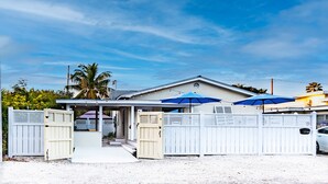 Een huis met een overdekte veranda, een hekpoort en een blauwe parasol.