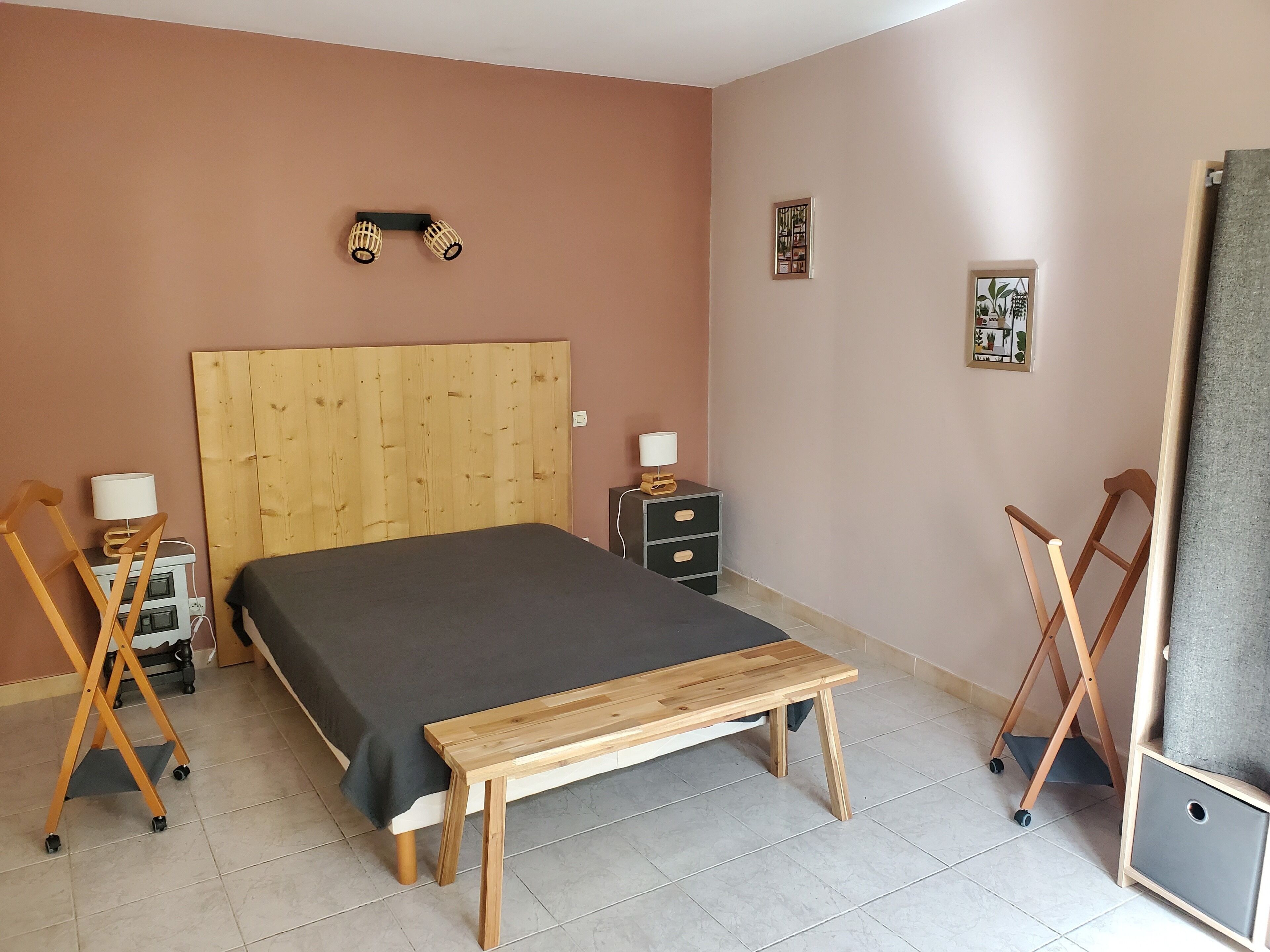 Une chambre à coucher avec un lit en bois, une table de chevet, une commode, une lampe et une petite étagère.