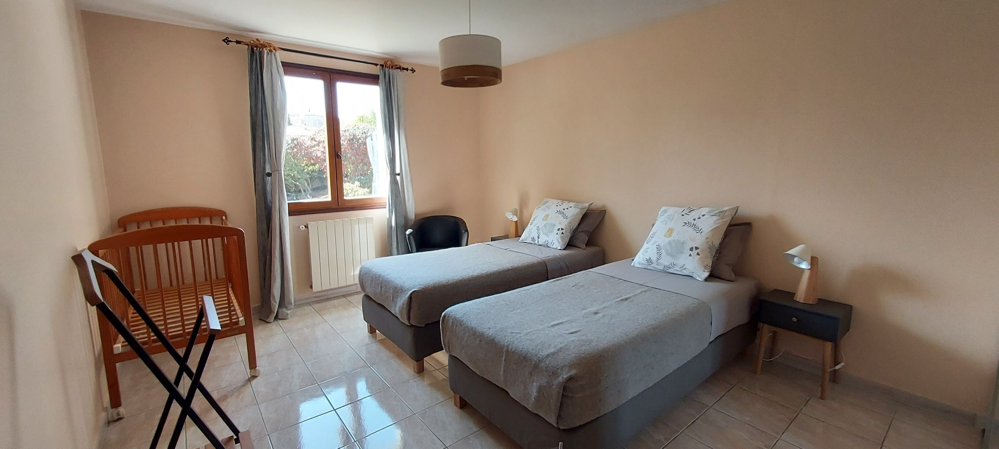 Une chambre avec deux lits, une chaise, une table de chevet et une fenêtre avec des rideaux.