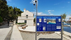 A coastal building with a signboard, a paved walkway, and a marina in the background. - Rustic House Miketa - Family Summertime (Preko)