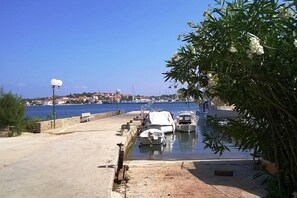 Un port de plaisance où sont amarrés des bateaux, un ciel bleu azur et, au loin, une vue sur une ville avec des bâtiments aux toits rouges.