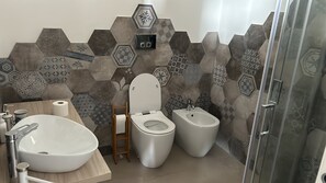 Un bagno moderno con un lavandino bianco ampio, un water e un bidet. Le pareti sono rivestite di piastrelle esagonali in diversi motivi.