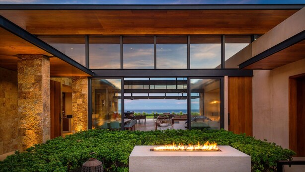A modern outdoor patio with a fire feature, stone walls, and a view of the ocean.