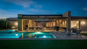 A modern house with a swimming pool, outdoor seating, and a covered patio area.