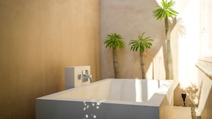 A modern bathroom with a freestanding bathtub, a shower, and two potted palm plants.