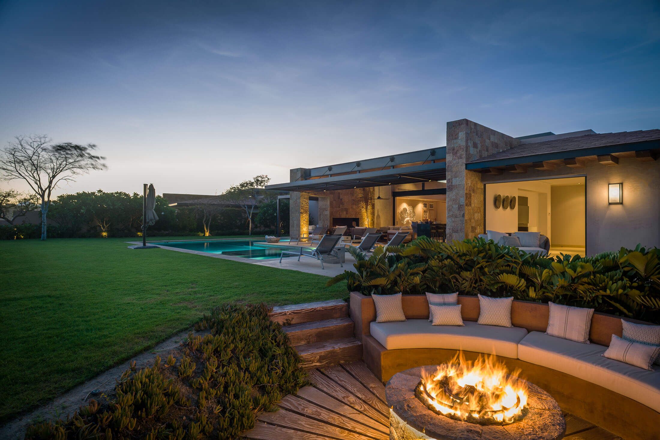 Un espacio exterior moderno con una chimenea, asientos al aire libre y una piscina.