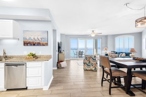 A modern kitchen with a dishwasher, a dining area with a table and chairs, and a view of the ocean through large windows. - Beach Colony East 14C- 3BD Gulf Front w/Beach Chair Service & Onsite Mgmt (Navarre Beach)