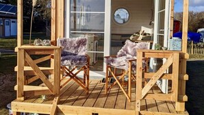 Een houten chalet met veranda, twee comfortabele fauteuils en een eethoek met tafel en stoelen.