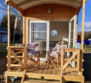 Eine Holzhütte mit Veranda, zwei bequemen Ohrensesseln und einem Essbereich mit Tisch und Stühlen.