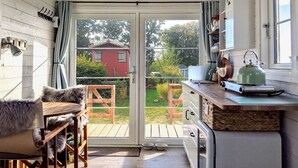 Een gezellige keuken met een schuifdeur die uitkomt op een houten terras, met een rood huis op de achtergrond.