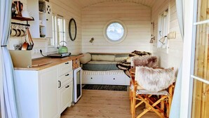 Een compacte kamer in chaletstijl met een kitchenette, een rond raam en een gezellige zithoek met een bont plaid.