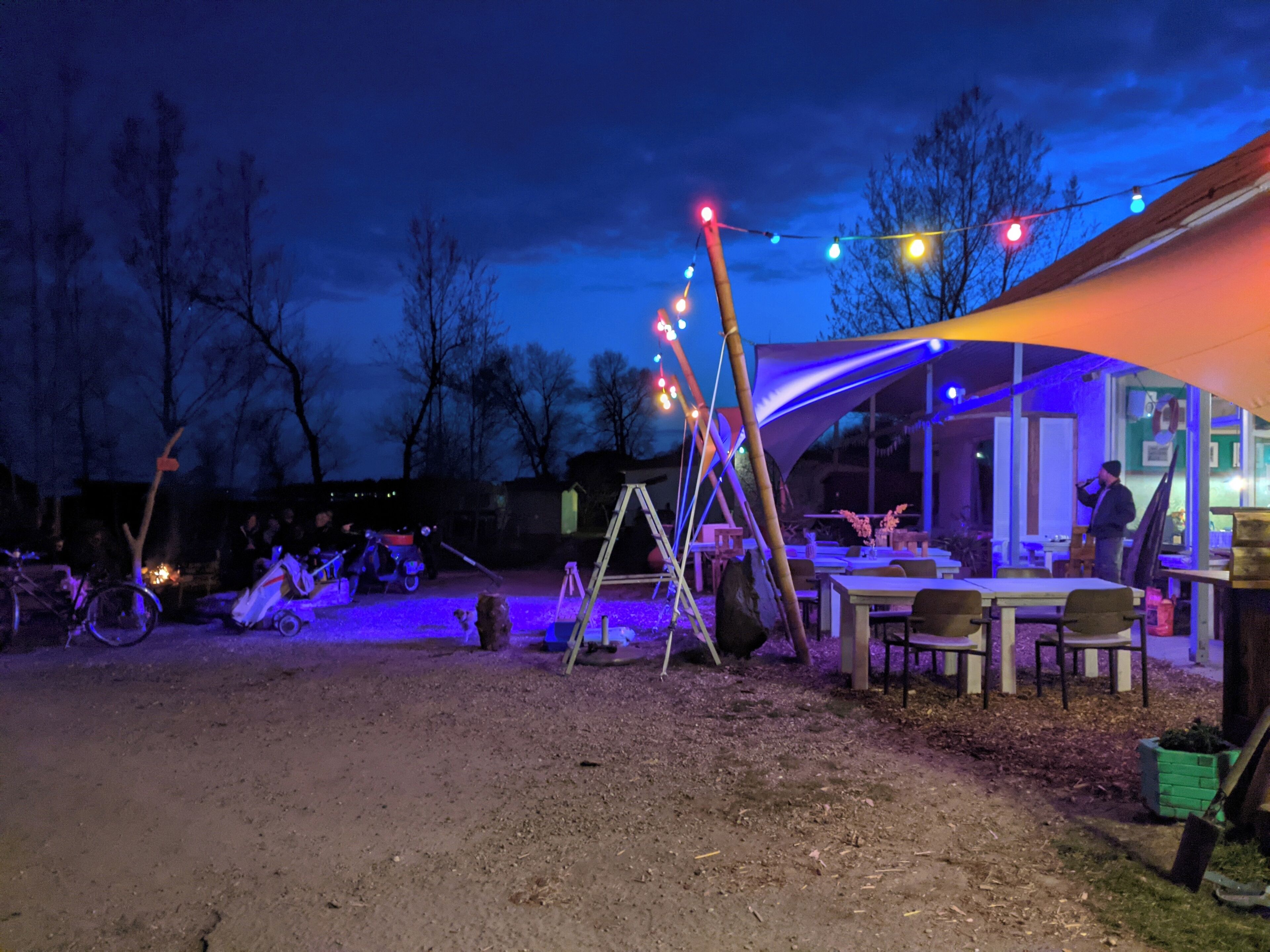 An outdoor dining area with tables and chairs, a tent, and string lights.