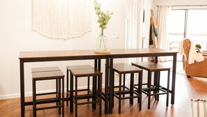 Et spiseområde med et træbord og fire ens stools. En vase med grønt løv står på bordet.
