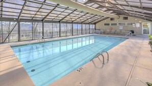 En indendørs swimmingpool med glasloft, krystalklart vand og en livredderstol.