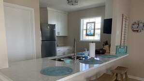 Una cocina con una isla grande, taburetes de madera, un refrigerador y una ventana con vistas.