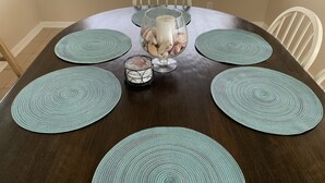 Una mesa de comedor con un cuenco de vidrio central que contiene adornos, rodeada por seis individuales color turquesa.