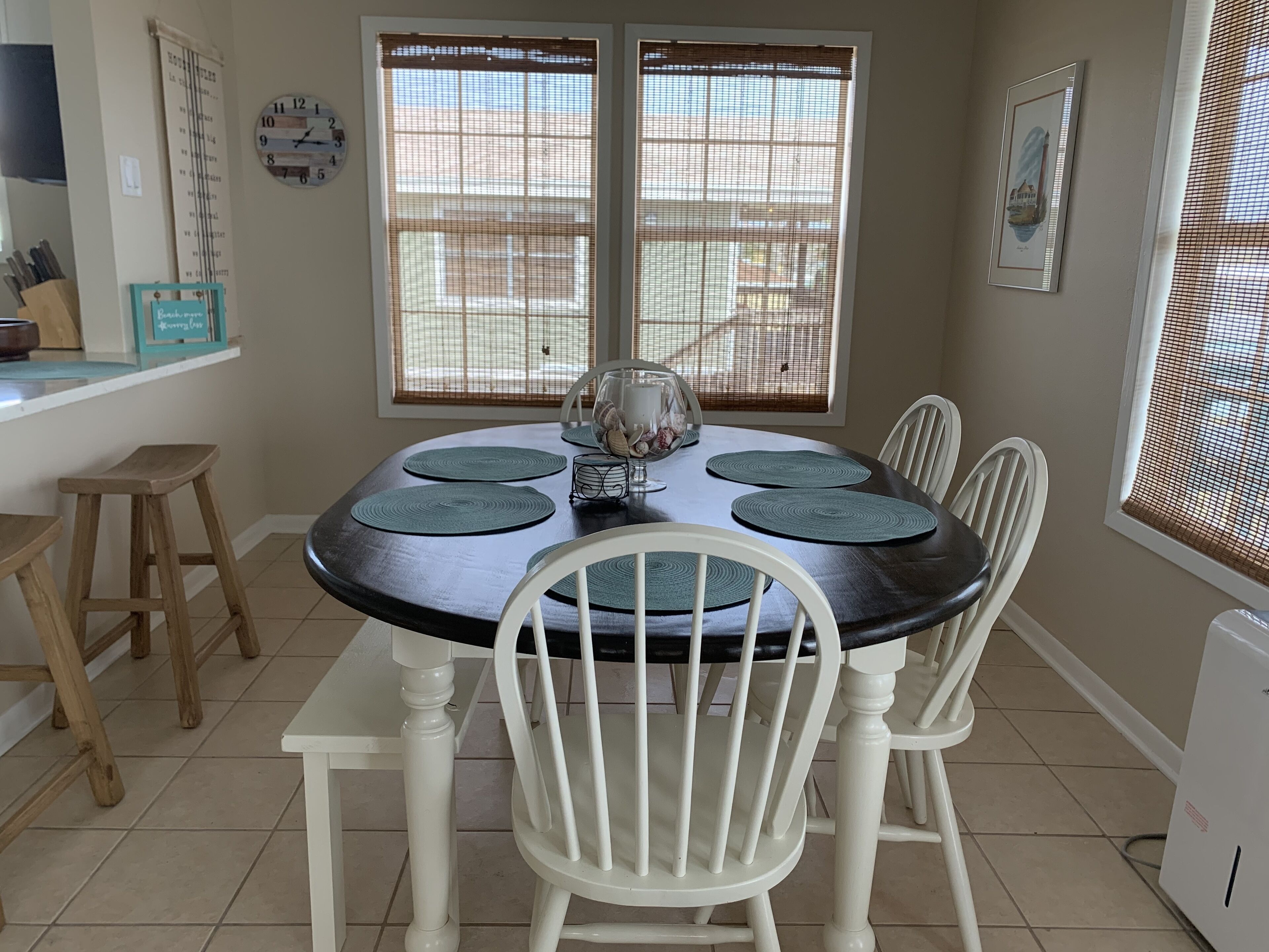 Un comedor con una mesa redonda, sillas blancas y una ventana con persianas.