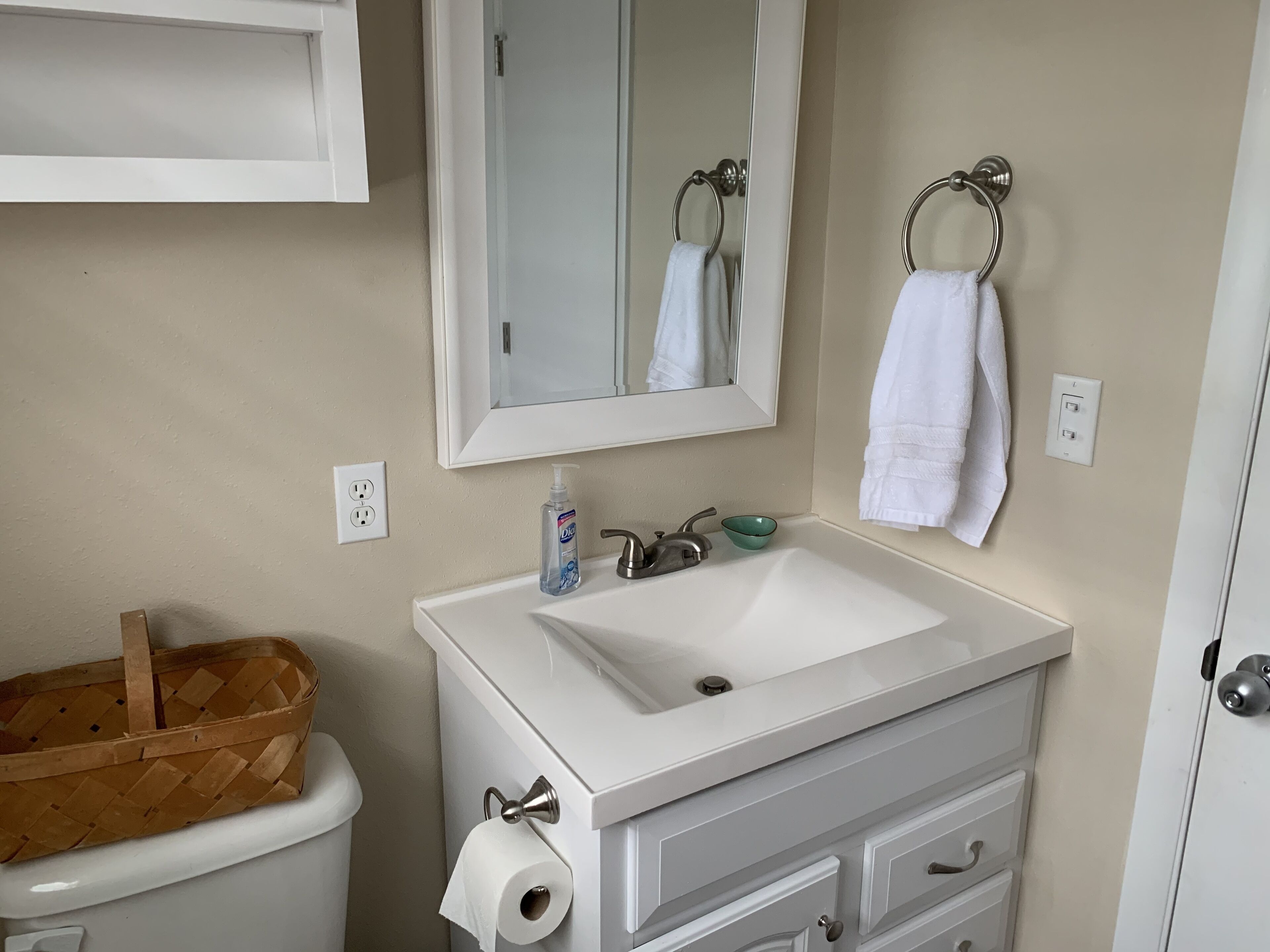 A bathroom with a white sink, a mirror, a toilet, and a basket.