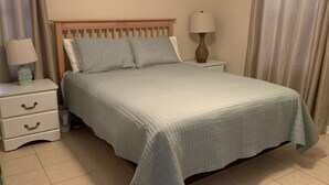 Una cama bien hecha con colcha acolchada, cabecera de madera, mesita de noche con lámpara y cómoda.
