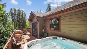 Une cabane en bois avec un jacuzzi sur la terrasse, entourée d’arbres.