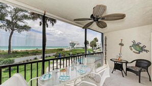 Ein Balkon mit Tisch und Stühlen, einem Deckenventilator und Blick auf Strand und Meer.