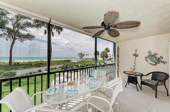 A balcony with a table and chairs, a ceiling fan, and a view of the beach and ocean. - Sunset Beach 102: Gulf Front, Stunning Views, On the Beach, Pool by Anna Maria Life Vacation Rentals (Holmes Beach)