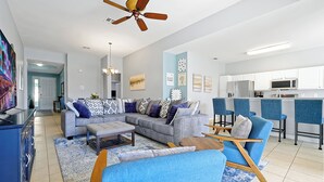 A modern living room with a grey sectional sofa, blue armchairs, a wooden coffee table, and a ceiling fan. - Windsor Hills Waterpark Community, NEW 2025 Game Room! Pool/Spa, Disney Rooms (Kissimmee)