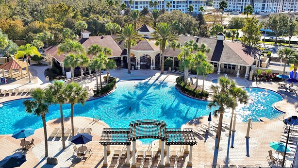 A resort with a large pool, palm trees, and a building in the background. - Windsor Hills Waterpark Community, NEW 2025 Game Room! Pool/Spa, Disney Rooms (Kissimmee)