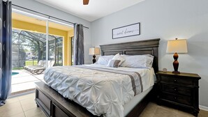A bedroom with a large bed, two bedside tables, a ceiling fan, and a view of the outdoors. - Windsor Hills Waterpark Community, NEW 2025 Game Room! Pool/Spa, Disney Rooms (Kissimmee)