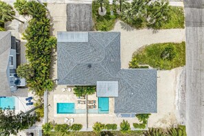An aerial view of a house with a large swimming pool, a covered patio, and a garden with palm trees.