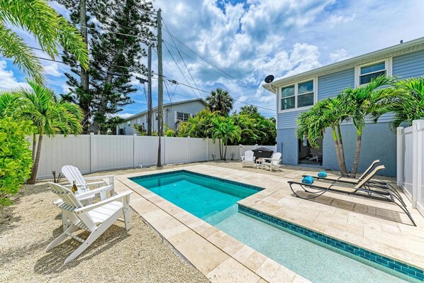 A backyard with a swimming pool, white deck chairs, and a barbecue area.